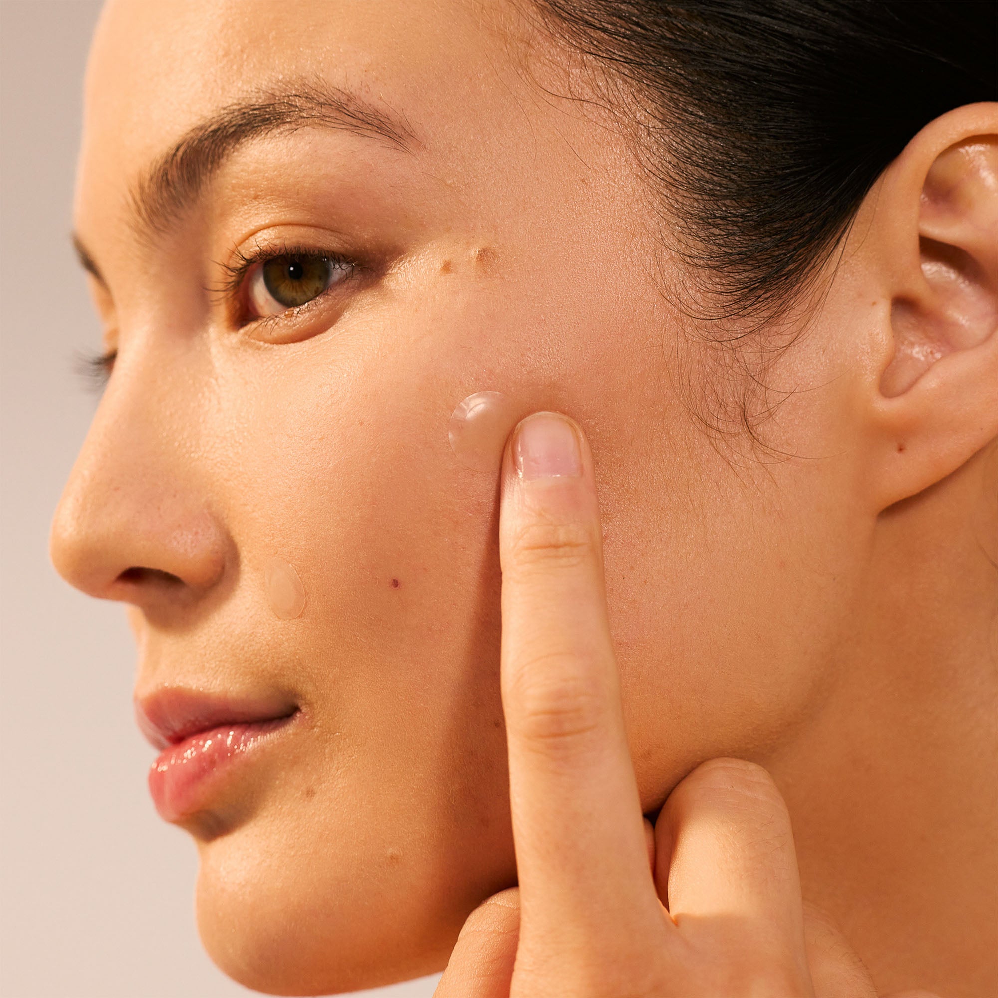 Close-up of a woman pointing to a blemish on her cheek.