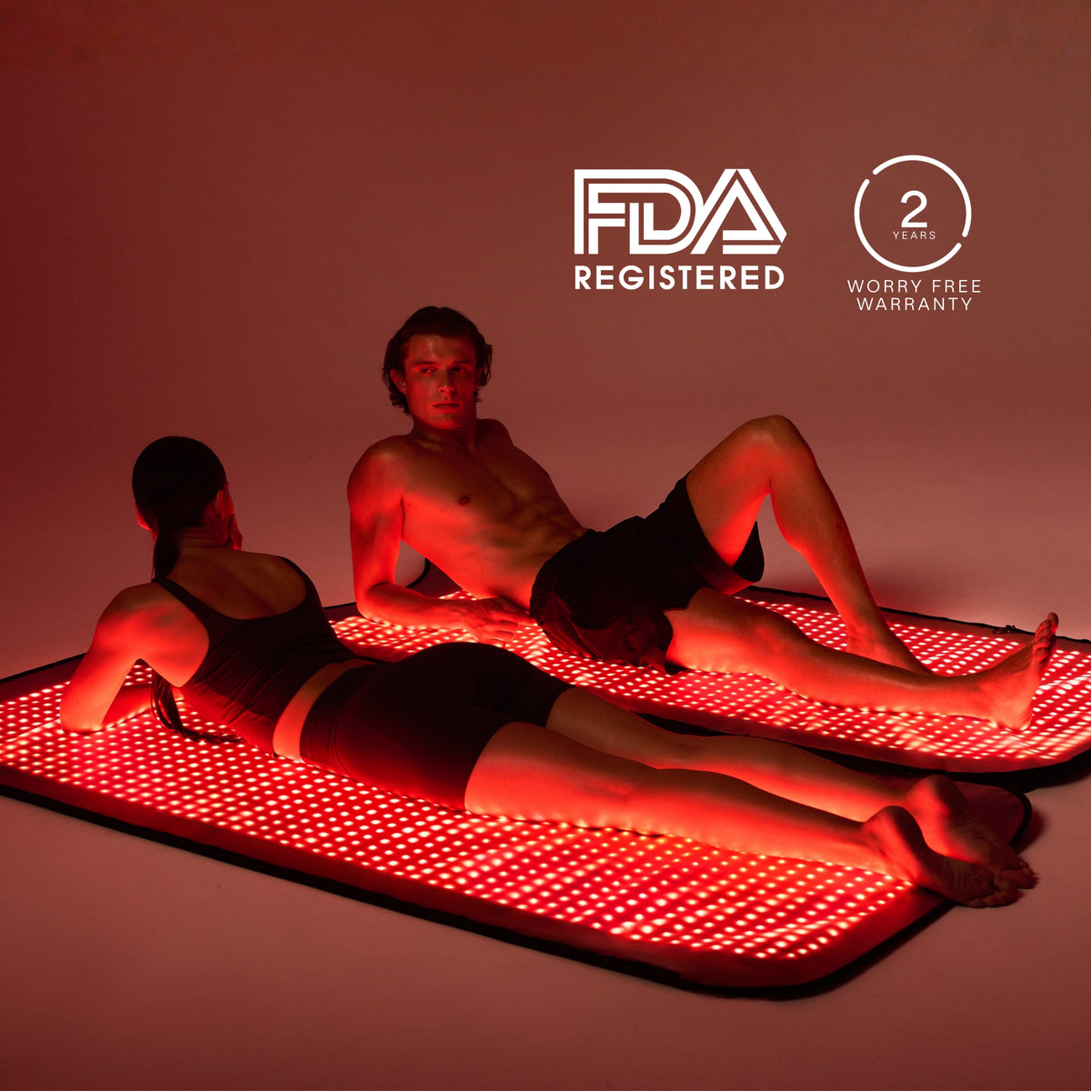 Two people reclining on separate illuminated Restora+ LED mats beside warranty and registration badges
