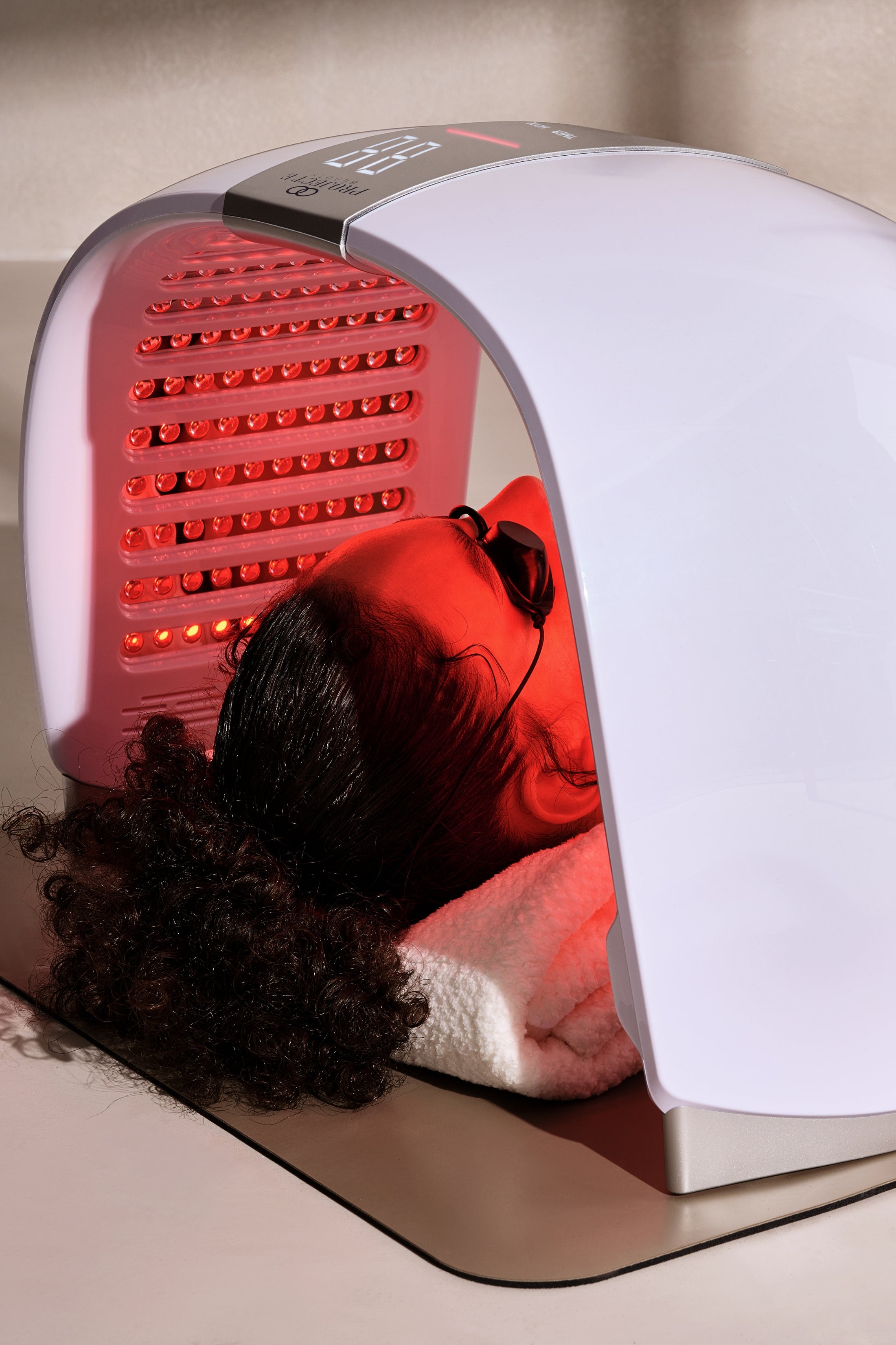 Woman using red LED light therapy dome for face.